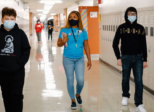 A site coordinator walking down a school hallway with two students
